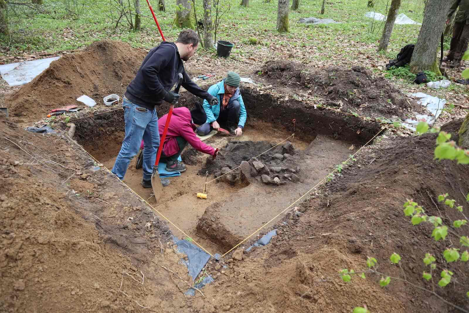 Doczyszczanie drugiego paleniska do zdjęcia, widać sznurek przecinający obiekt na pół (linia profilowa). Doczyszczają trzy osoby.