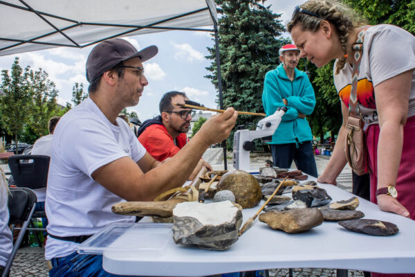 _DSC6427 edukator okazuje rekonstrukcję strzały pradziejowej, na stole narzędzia krzemienne, w tle słuchacze