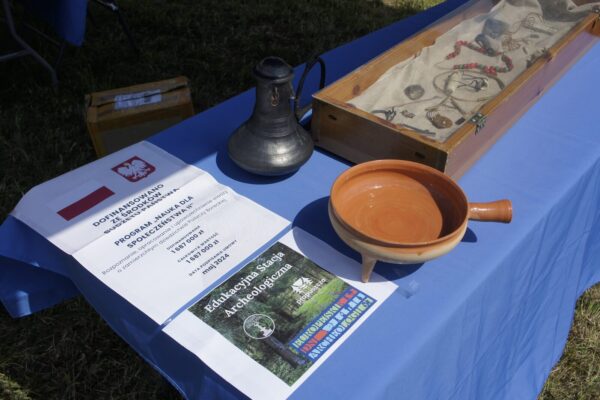 _DSC6573 (1) stół edukacyjny, a na nim plakaty promujące Edukacyjną Stację i projekt Prapuszcza, repliki naczyń ceramicznych oraz gablotę z wystawą archeologiczną