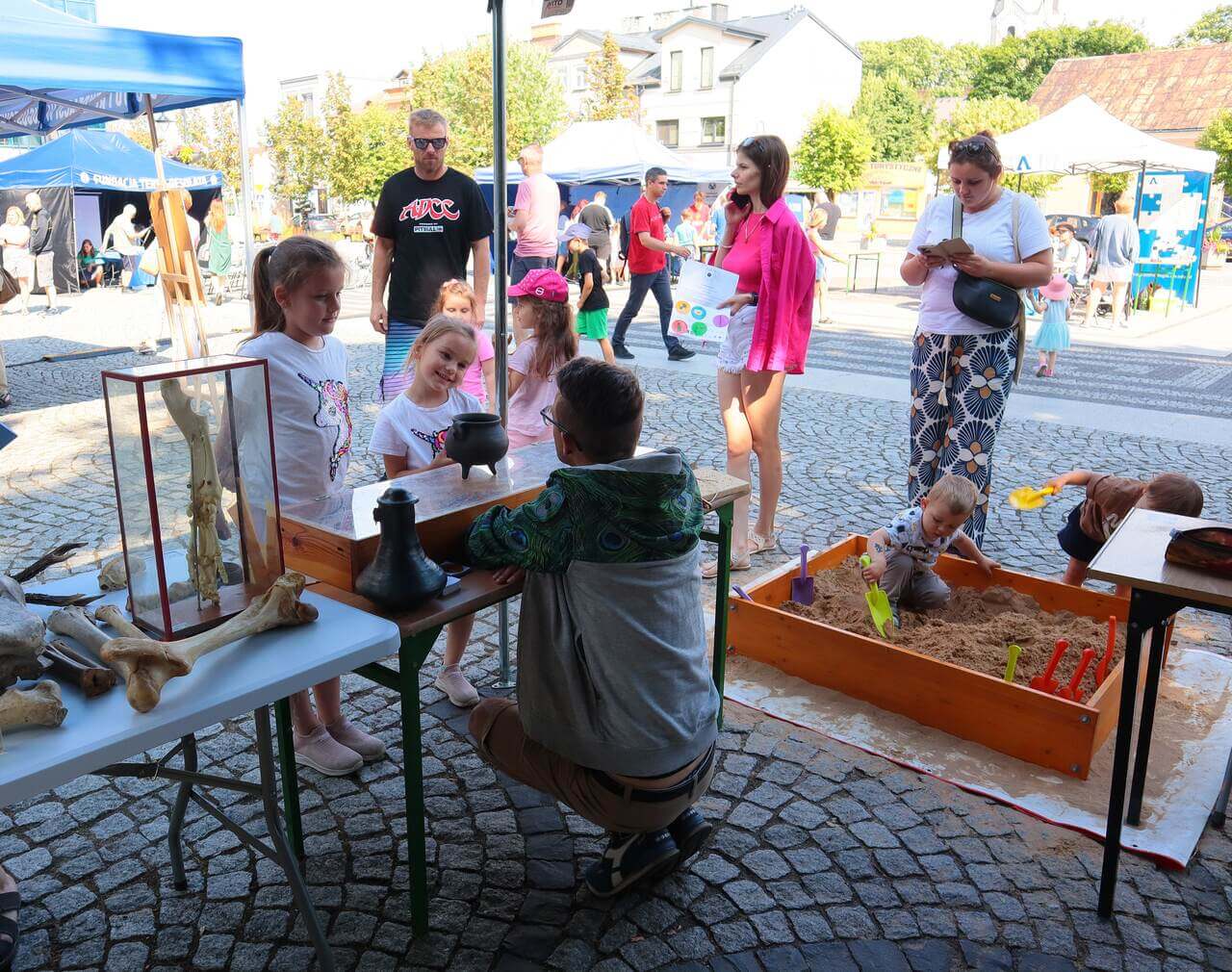 dzieci rozwiązują zagadki od edukatora na stoisku archeologicznym, obok inne bawią się w piaskownicy