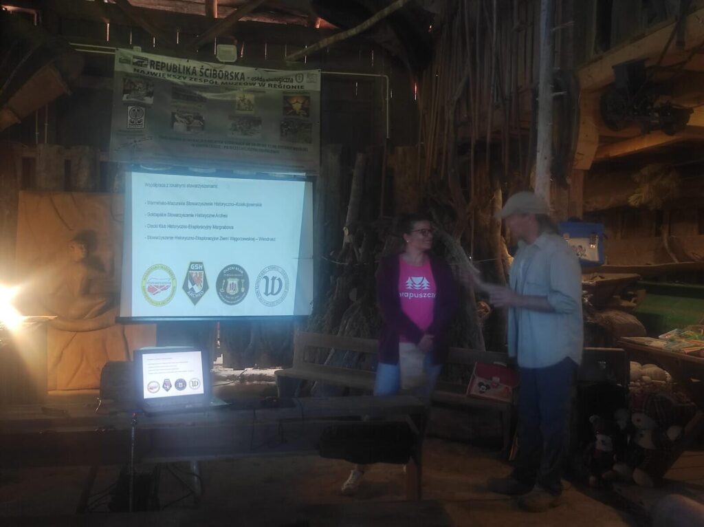 Iwona wygłasza referat, widać na prezentacji logotypy grup poszukiwaczy z nami współpracyjących