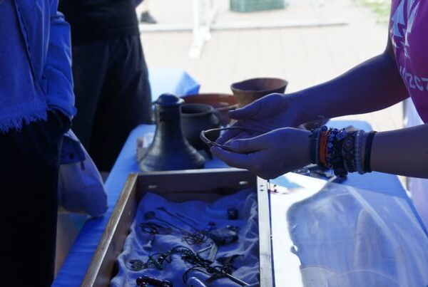 zbliżenie na ręce edukatorki pokazującej naszyjnik z brązu nad gablotą