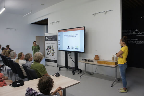 Iwona i Emilia stoją po dwóch stronach ekranu wyświetlającego prezentację