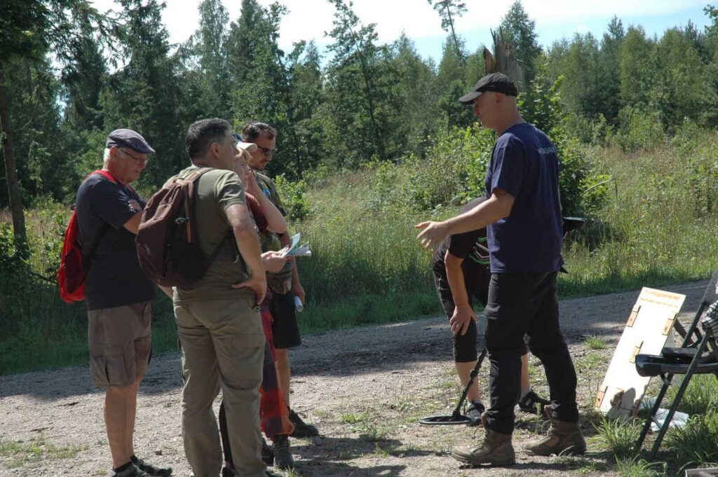 Konrad omawia graczom zadanie na swoim stoisku dot. wykrywaczy