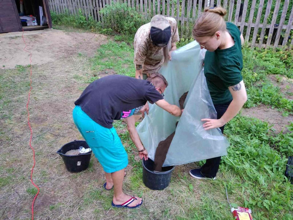 3 osoby przesypują glebę na sito z folii