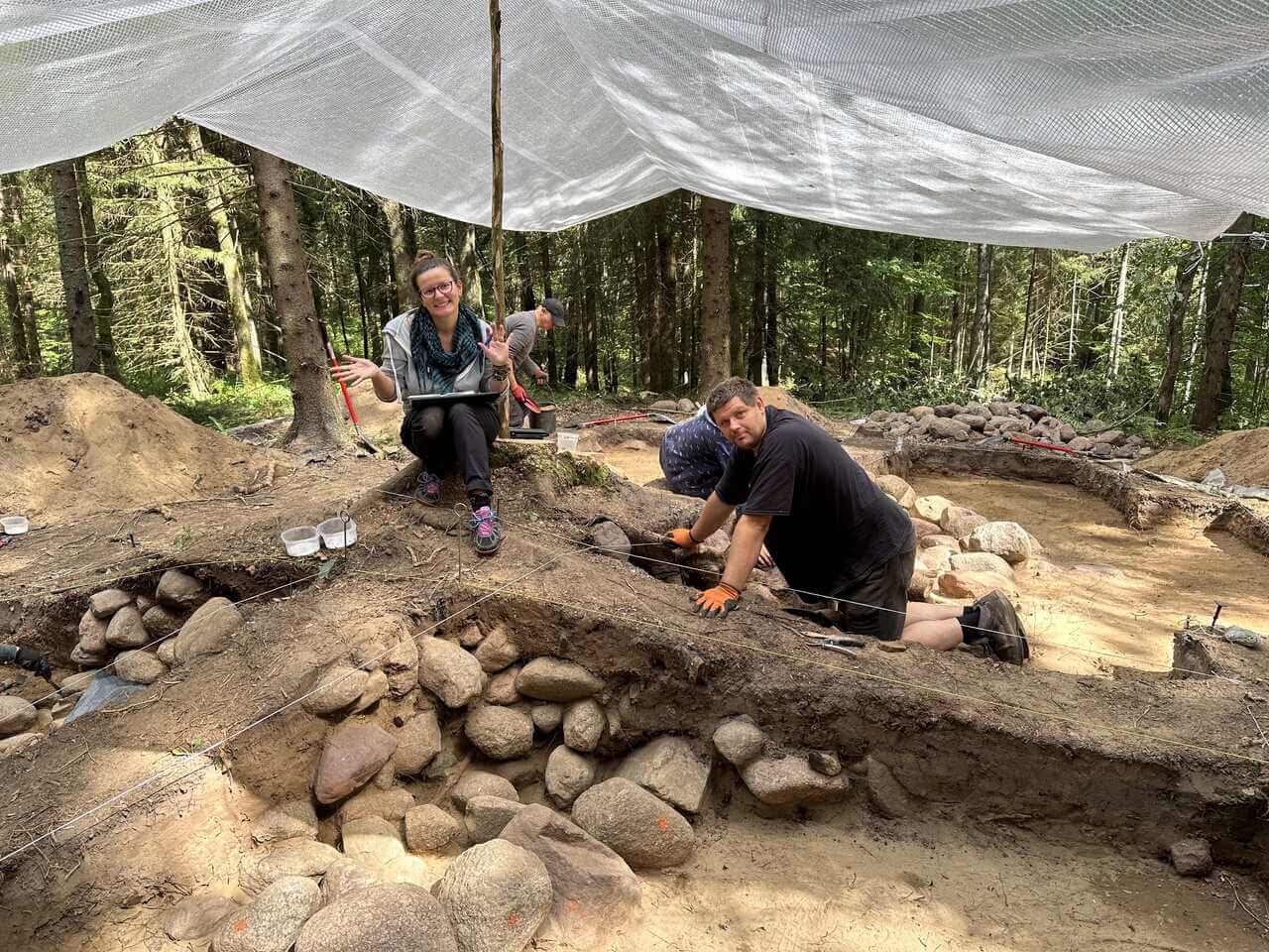 Archeolodzy odczyszczają kurhan, kierownik wykopalisk stoi i zapisuje pomiary