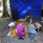 edukatorka pomaga dzieciom poszukiwać ukrytych zabytków w piaskownicy archeologicznej