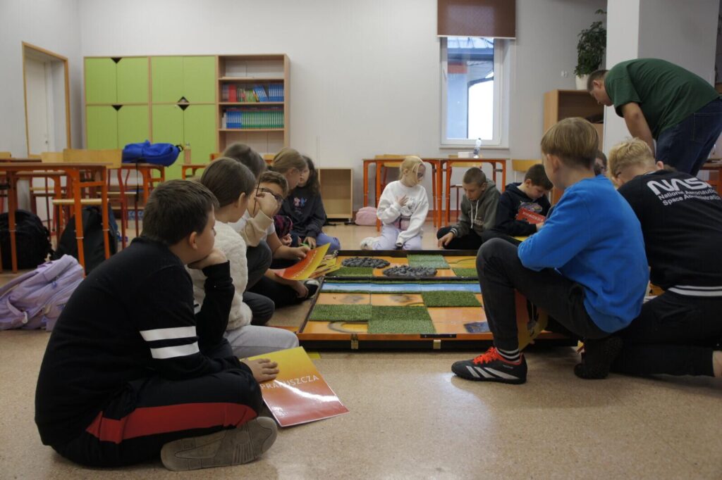Ucznowie siedząc nad planszą rozmawiają o grze