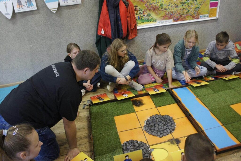 Edukator i gracze pochylają się nad planszą podczas rozgrywki.