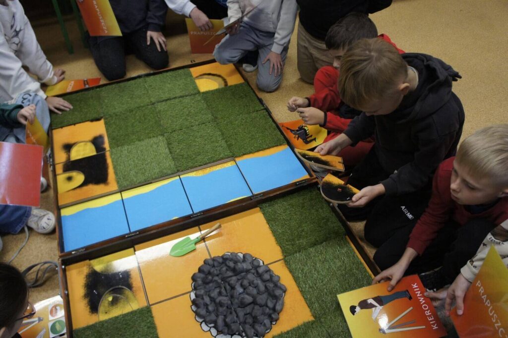 Uczniowie siedzą wokół planszy i grając odkrywają poszczególne warstwy.