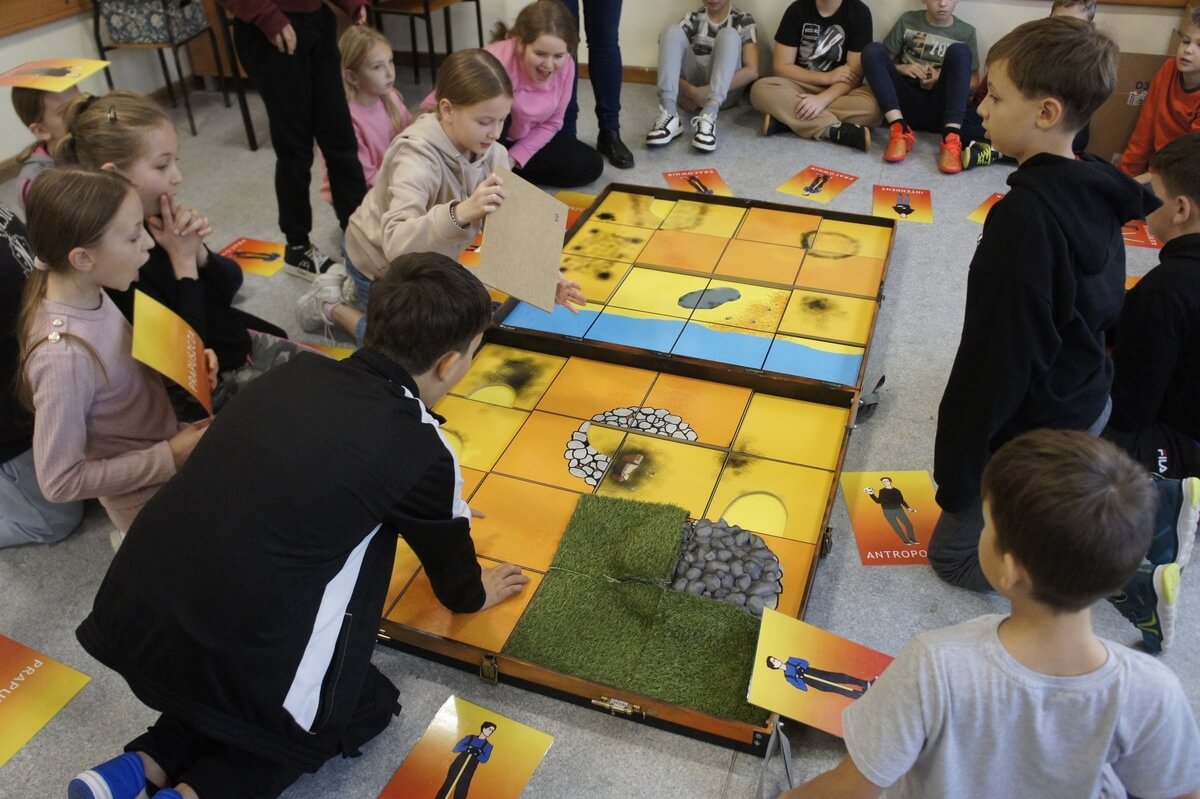 Uczniowie pochylają się nad planszą gry odkrywając poszczególne elementy kolejnych warstw stanowiska
