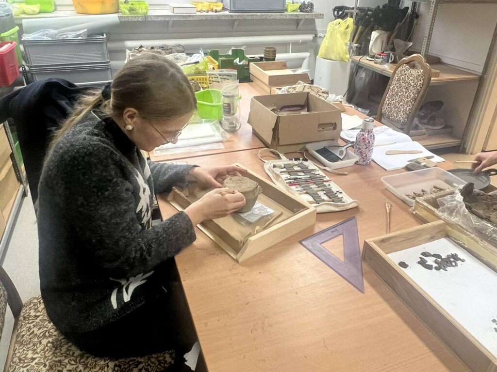 Agata eksploruje małe naczynko przystawkę, odkryte na wykopaliskach obok urny.