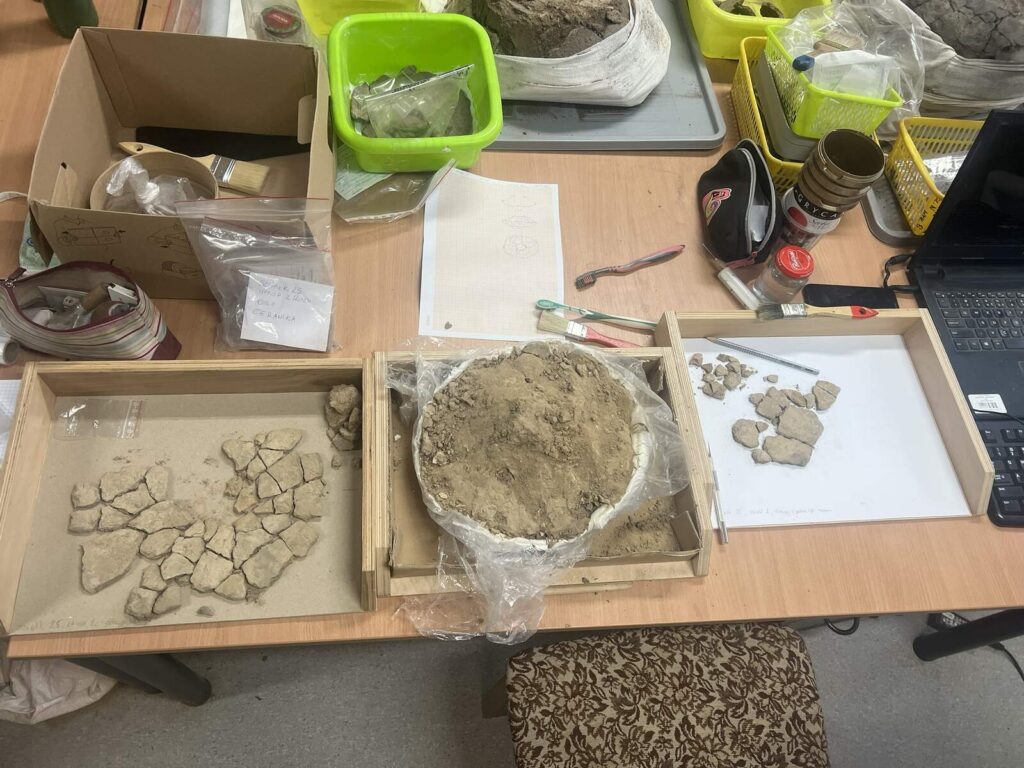 Widok z góry na urnę i zdjętą warstwę naczynia, które w górnej części pokruszyło się po zgnieceniu ziemią.