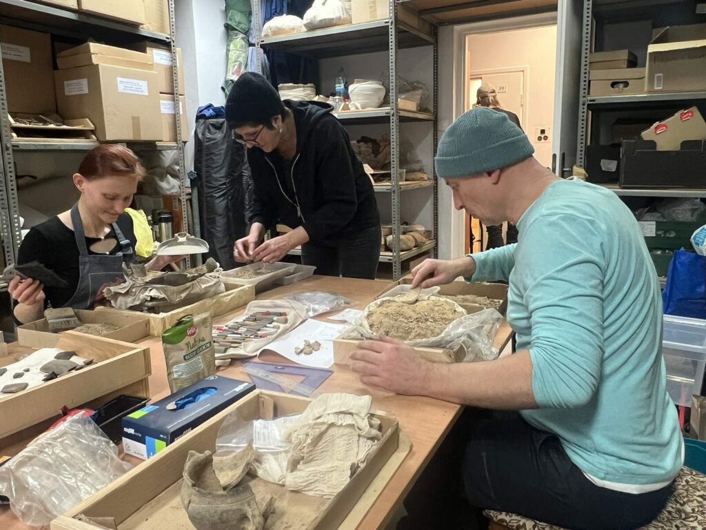 Vini, Agata i Konrad eksploruja urny i wybierają fragmenty naczyń i kości.