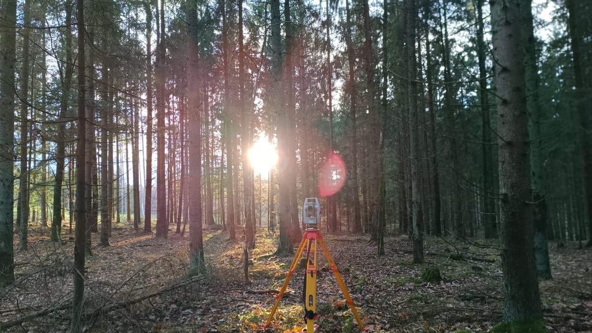 Widok na las i prześwitujący zachód słońca, na pierwszym planie stoi tachimetr.
