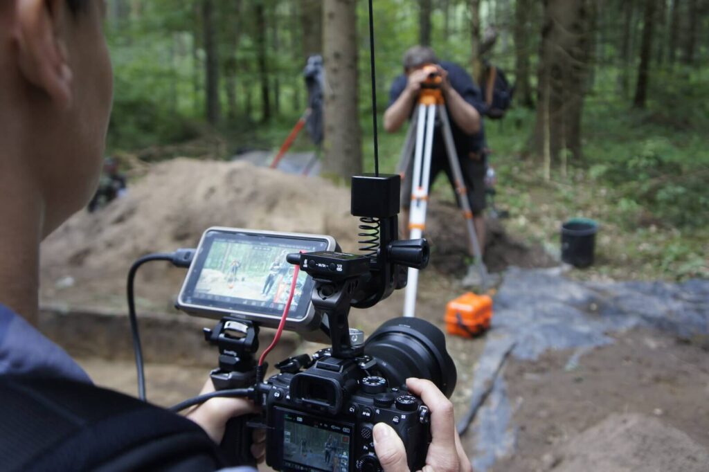 Pierwszy plan: zbliżenie na kamerę i wyświetlacz, drugi plan: Piotrek odczytuje wysokość z niwelatora