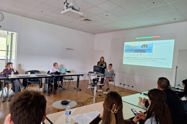 IMG-20250315-WA0008_Easy-Resize.com Agata i Iwona przedstawiają referat, na pierwszym planie siedzący słuchacze