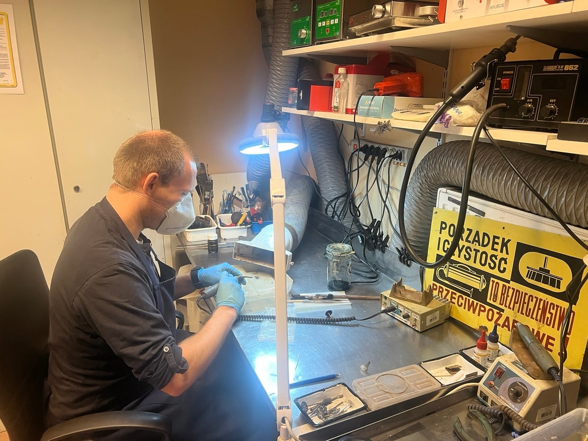 Widzimy siedzącego Macieja przy stanowisku do konserwacji. Oczyszcza kolejny zabytek metalowy.