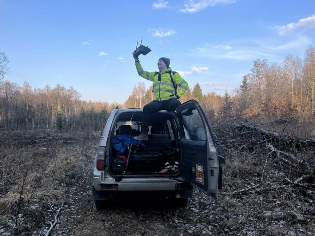 Operator drona siedzi na dachu auta, by lepiej łączyć się z urządzeniem.
