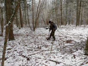 Członek ekipy z wykrywaczem przemierza las przyprószony śniegiem