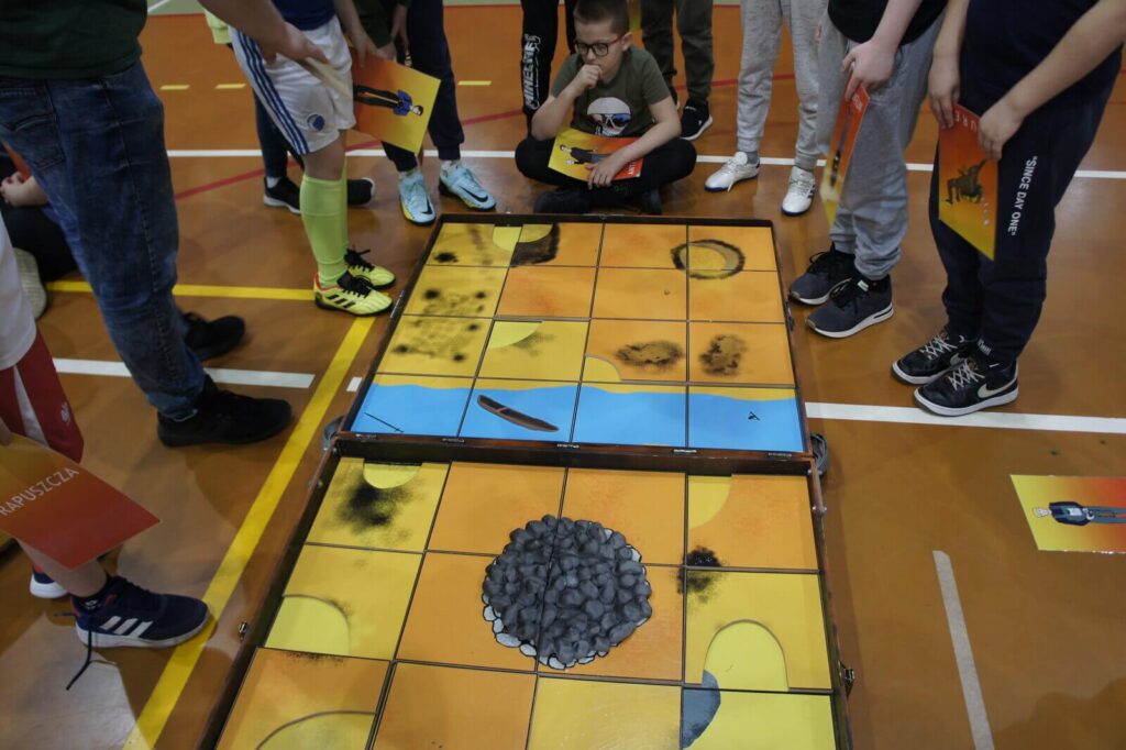 Gracze stoją nad odkrytą planszą gry.