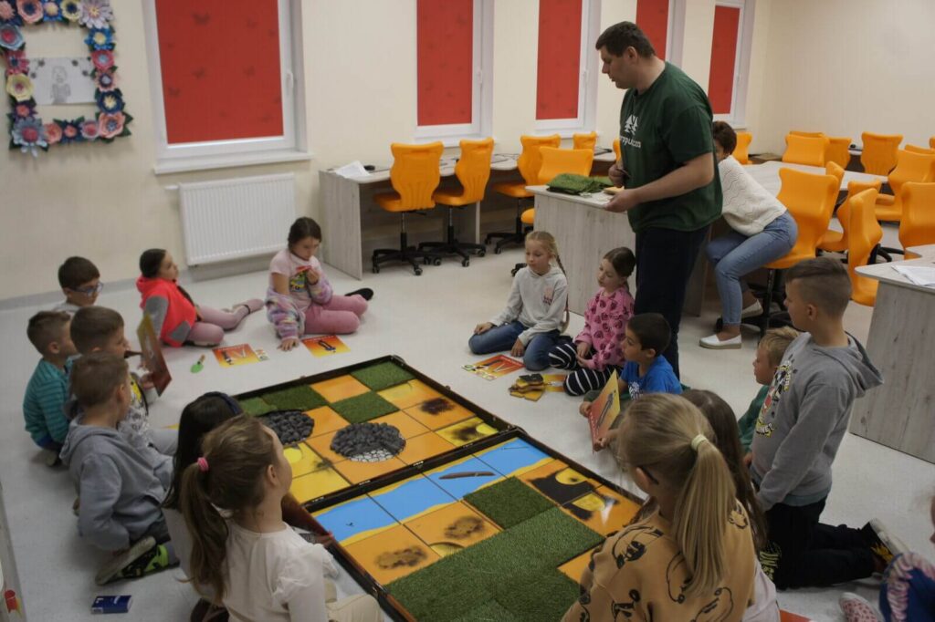 Edukator tłumaczy coś graczom siedzącym wokół planszy