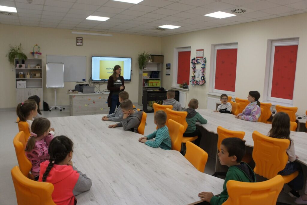 Edukatorka opowiada o pracy archeologa uczniom siedzącym przy dużych stołach