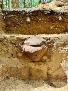 Stożkowate naczynie z pokrywką sfotografowane w profilu w ziemi.