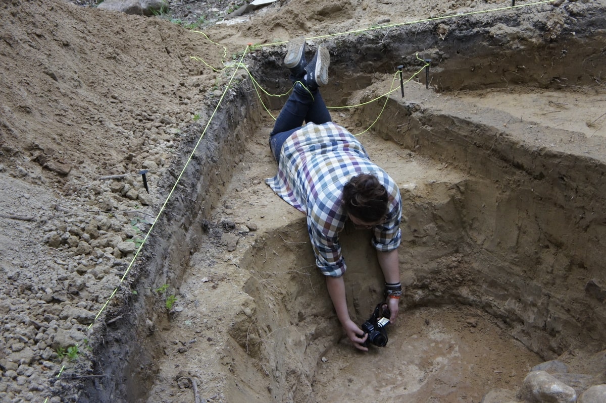 Iwona leżąc robi zdjęcie profilu obiektu w wykopie.