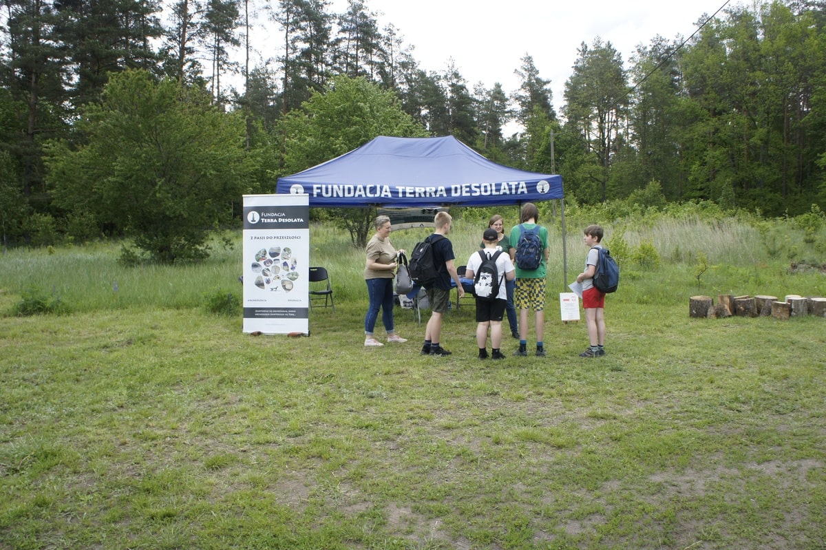 Monika tłumaczy graczom zasady gry, w tle namiot.