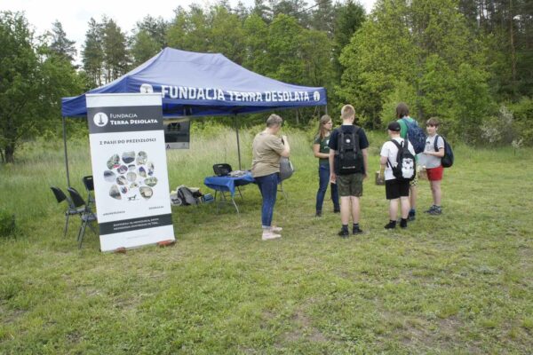Punkt startowy: Monika tłumaczy zasady gry pierwszej drużynie, w tle namiot i logo fundacji.