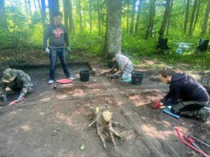Kilka osób eksploruje obiekt tj. palenisko z kamieni.