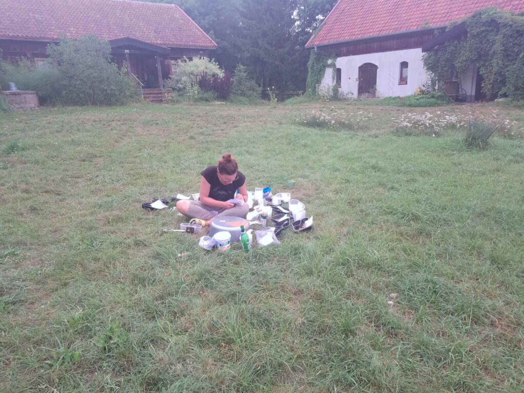 Iwona siedząc na podwórkowej trawie opisuje umyte i oczyszczone artefakty (ceramika, kości, próbki).