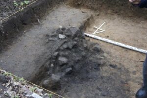 Odczyszczona połówka paleniska, widoczne małe kamienie i ciemna ziemia