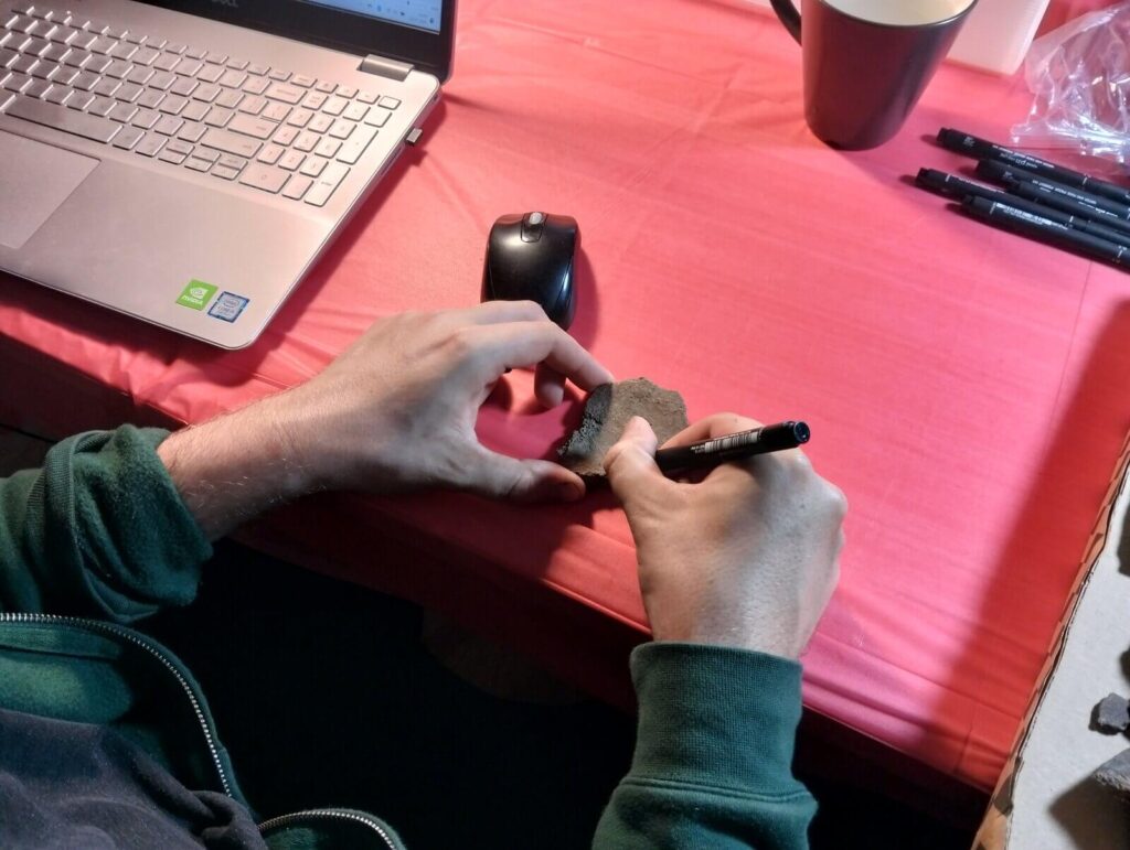 Zbliżenie na moment podpisywania fragmentu ceramiki przy użyciu cienkopisu.