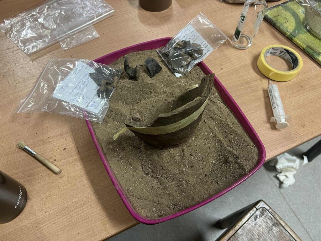 Sklejone fragmenty naczyń stoją w pojemnikach z piaskiem.