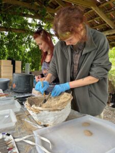 Mela czyści wnętrze popielnicy pędzlem, za nią stoi Monika, antropolog