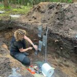 dr Cywa kucając w wykopie wbija tzw. rynienki w profil jamy do pobierania monolitów.