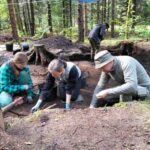 Dwie osoby eksplorują plan wykopu, a dr hab. Poręba pobiera próbkę.