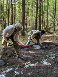 Dwie osoby pochylone z łopatami plantują wykop (wybierają cienką warstwę ziemi).