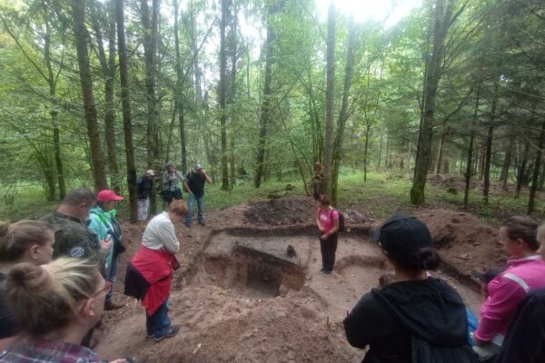 IMG_20250906_113721379_MFNR_Easy-Resize.com Grupa przygląda się otwartemu wykopowi archeologicznemu na osadzie bałtyjskiej. Widać profil obiektu.