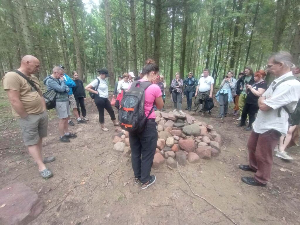 Edukatorka opowiada o kurhanach stojąc nad jednym z zrekonstuowanych przez fundację.