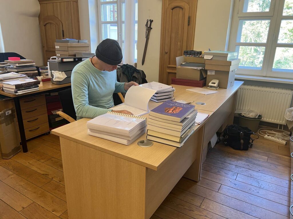 Konrad siedząc przy biurku przegląda publikacje muzealne.