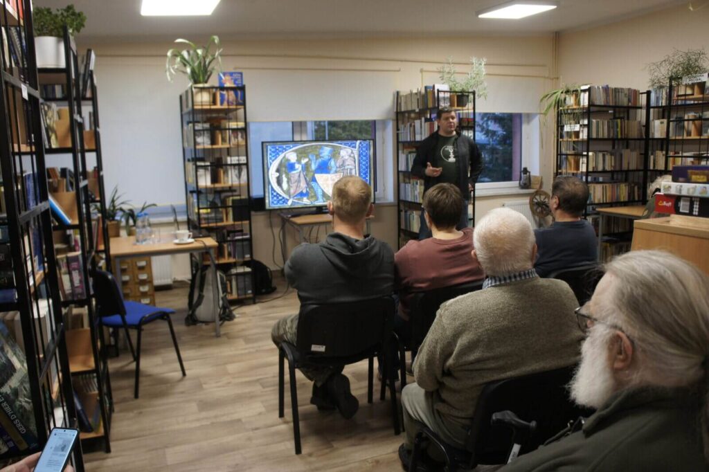 Widok z tyłu sali na słuchaczy i Piotra prowadzącego wykład.