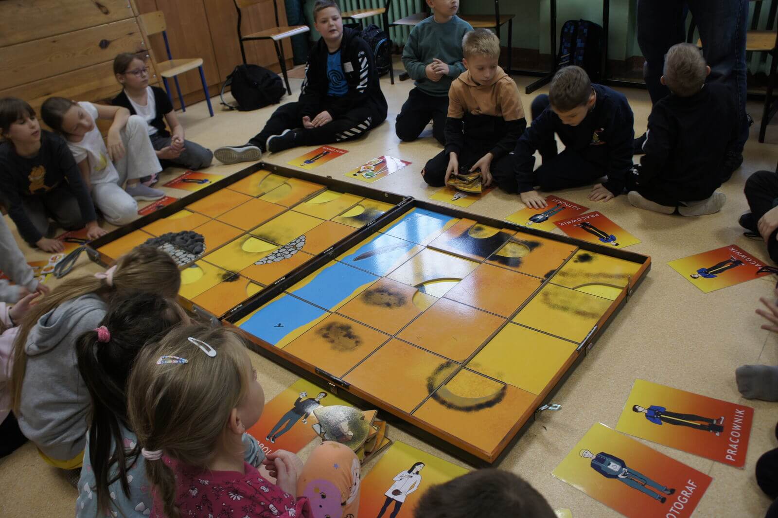 Grupa uczniów siedzi wokół planszy, każdy ma przed sobą swoją kartę postaci.