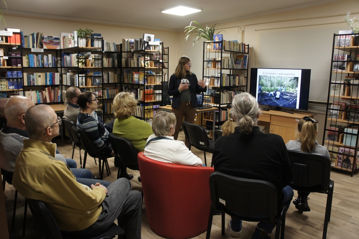 Widok na siedzących słuchaczy i prelegentkę omawiającą slajd prezentacji.