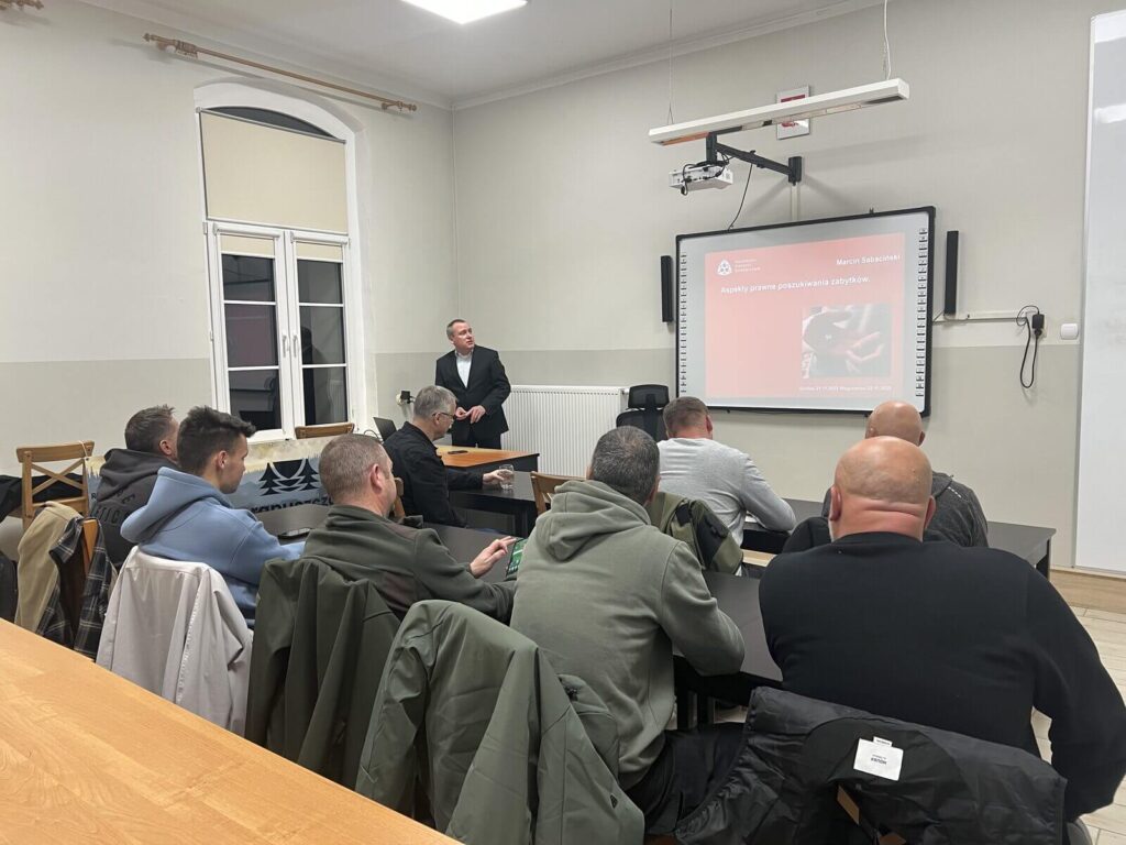 Widok z tyłu sali na siedzących słuchaczy i prelegenta.