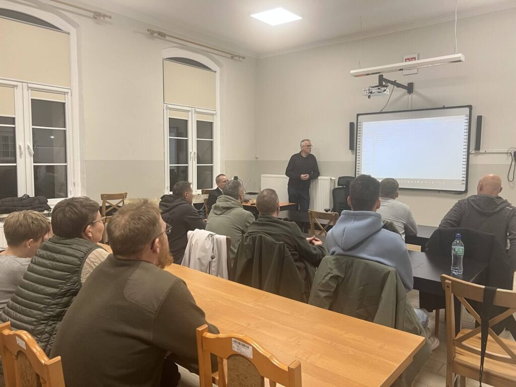 Goście siedząc w ławach słuchają wykładu.