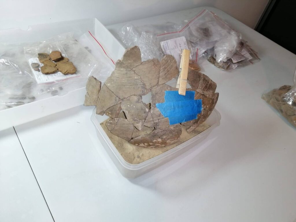 W pojemniku z piaskiem stoi sklejony fragment naczynia