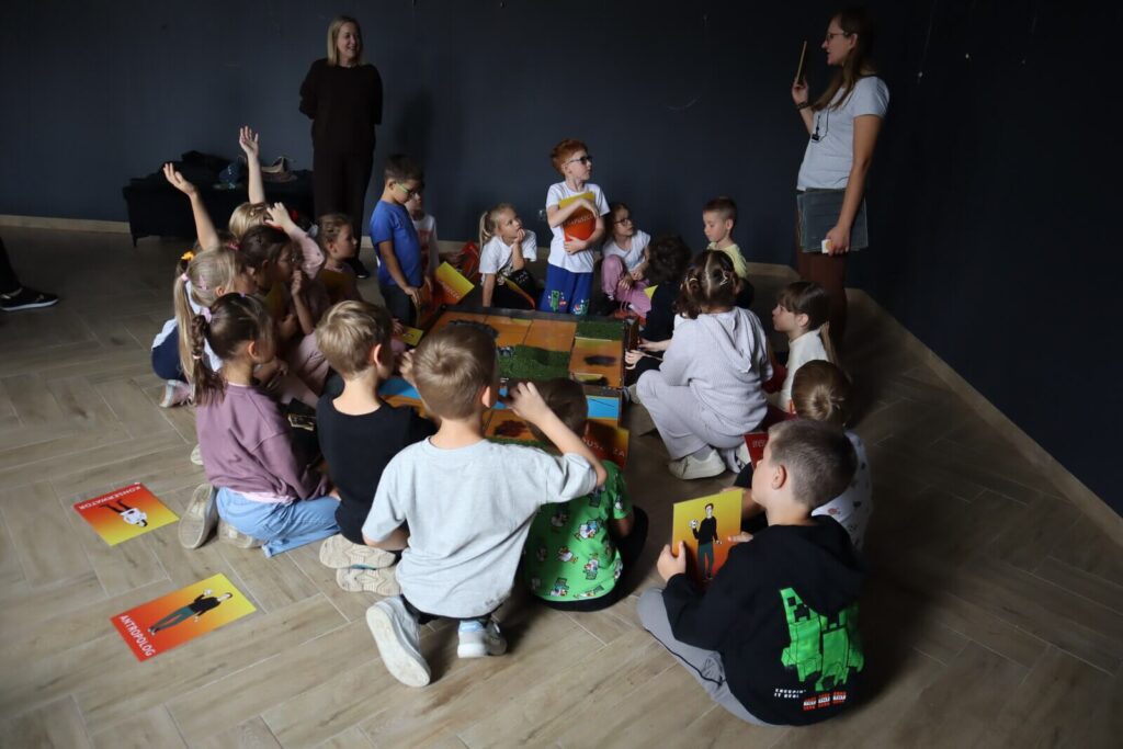 Dzieci grają w wielką grę planszową Prapuszcza pod okiem edukatorki